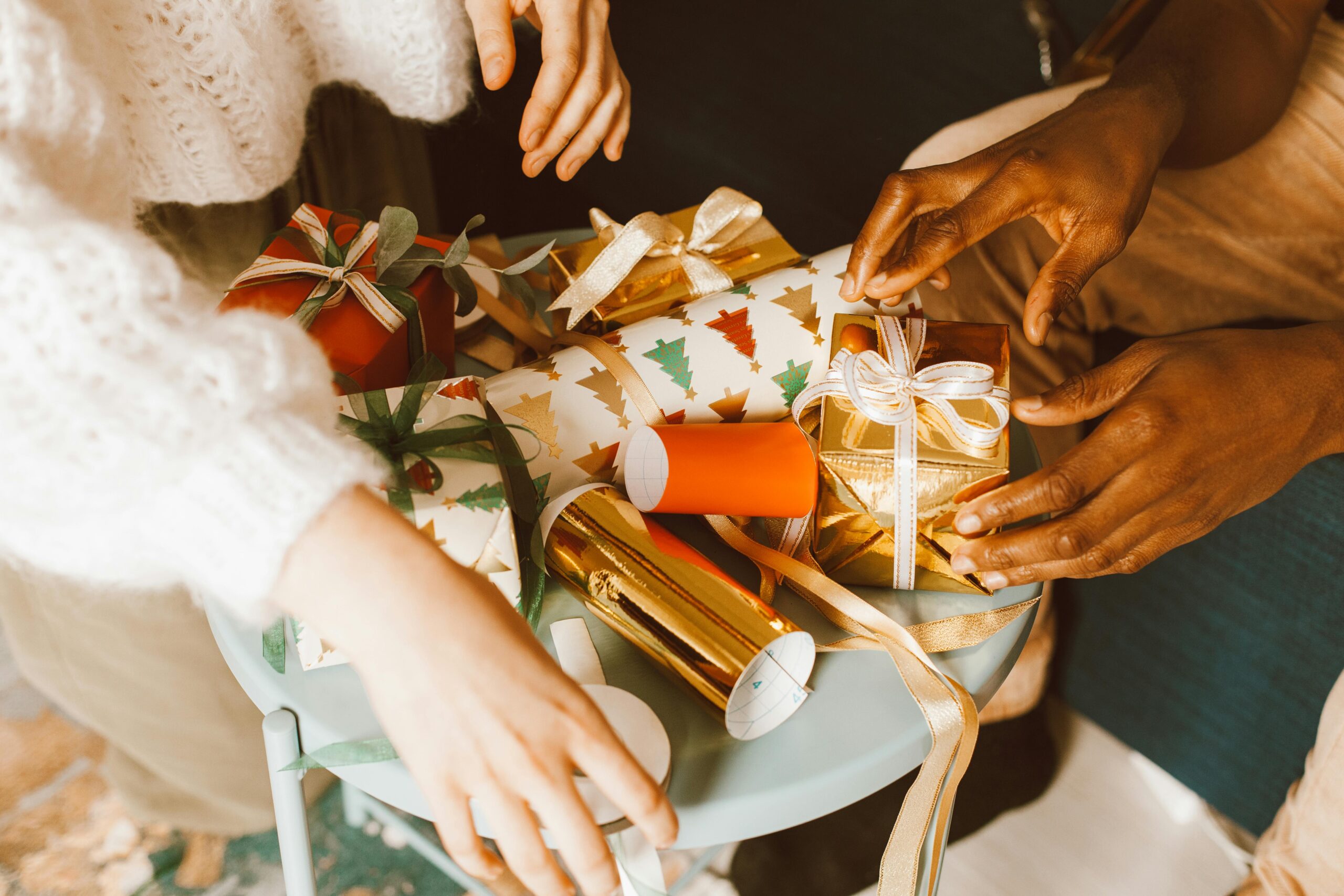 Hands preparing Christmas gifts with colorful ribbons and wrap.